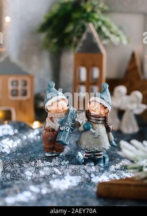 Porzellan Figuren der Kinder in eine weihnachtliche Dekoration. Winter Figuren der ein Junge und ein Mädchen mit den Geschenken, die auf dem Hintergrund der Häuser und Kegel. Weihnachten Stockfoto