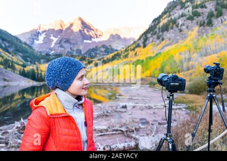 Maroon Bells See in Aspen, Colorado im Herbst bei Sonnenaufgang mit Frau kalt mit Hut stehend durch Kameras auf Stativen Stockfoto