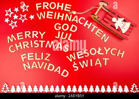 Aufschrift Frohe Weihnachten in Deutsch, Englisch, Polnisch, Schwedisch und Spanisch, liegend von oben. Von Holz- Inschriften, auf einem roten Bac isoliert Stockfoto