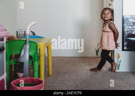 Lächelnd 2 Jahre alten multirassischen stehendes Mädchen barfuß auf dem Teppich von Wand Stockfoto