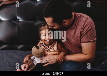 Vati hält 2 Jahre alten multirassischen Tochter mit Puppe lächelnd Stockfoto