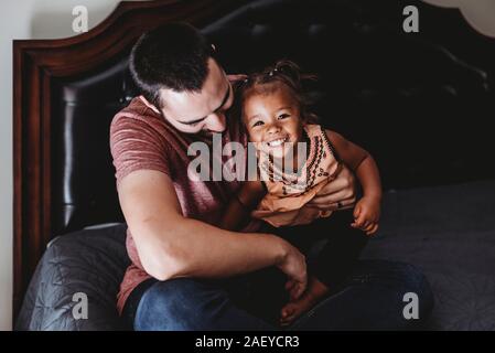 Dunkelhaarige Vati sitzen auf dem Bett mit einem Lächeln Multirassischen 2 Jahre alt Stockfoto