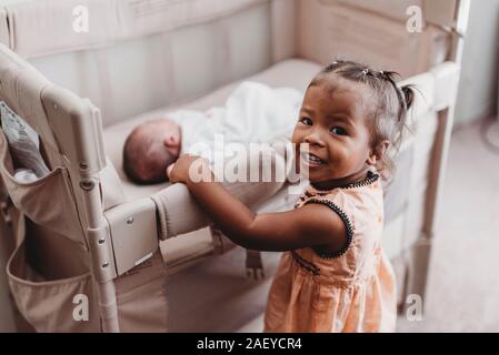 Lächelnd Multirassischen 2 Jahre alten Holding Krippe der schlafenden Baby Schwester Stockfoto