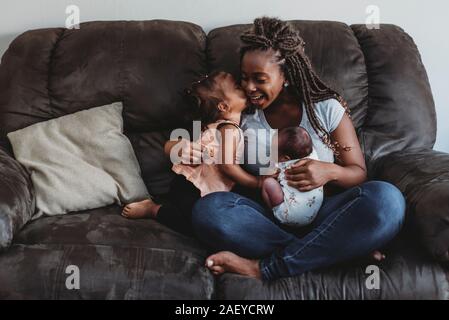 Multirassischen 2 Jahre alten küssen Mutter Leitkiel mit schleifer holding newborn auf der Couch Stockfoto