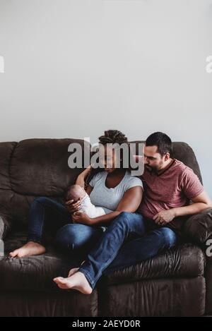 Barfuß gemischtrassiges Paar auf der Couch lächelte gepuckte Kleinkind Stockfoto