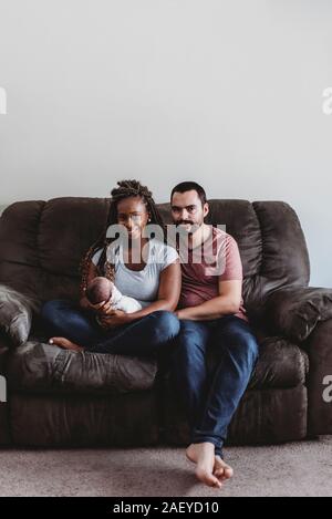 Gemischtrassiges Paar hält gepuckte Neugeborenen beim Sitzen auf der Couch Stockfoto