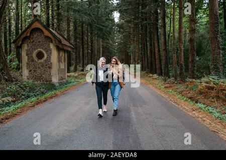 Zwei Frauen gehen auf einem Weg im Wald, während Ihr Telefon beobachten Stockfoto