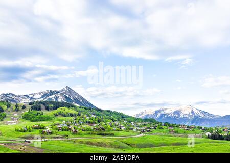 Mt Crested Butte Panoramablick Snow Mountain View mit bewölktem Himmel in üppigen, grünen Gras Sommer mit Häusern, Gebäuden in kleinen Stadt Dorf Stockfoto