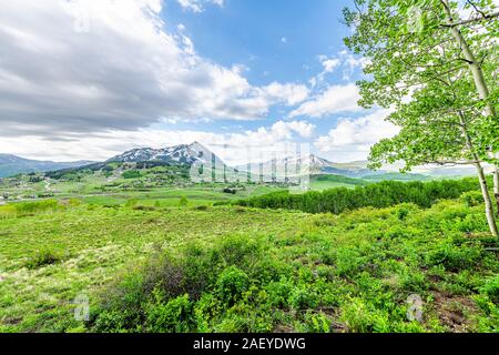 Mount Crested Butte Snow Mountain View mit bewölktem Himmel in üppigen, grünen Gras Sommer mit Aspen Bäume und Häuser Gebäude in der kleinen Stadt Dorf Stockfoto