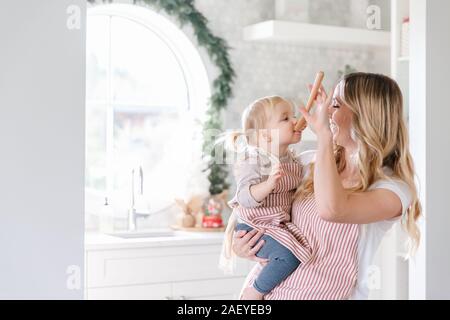 Mutter Holding baby Tochter in passenden Schürzen backen in der Küche Stockfoto