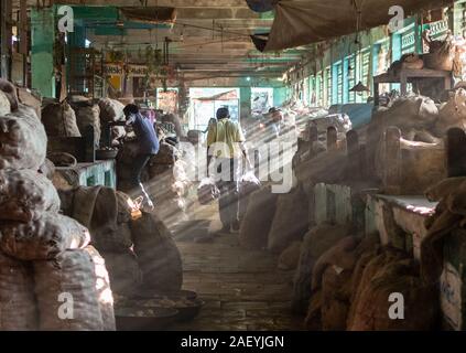 Hinteres Profil eines Mannes, der mit zwei Säcken Zwiebeln auf dem staubigen, alten Gemüsemarkt von Bhavnagar spazieren ging. Stockfoto