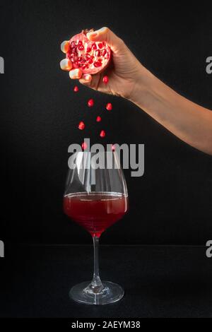 Frau Hand geschnitten Granatapfel und Samen in ein Glas Granatapfel Wein fallen Stockfoto