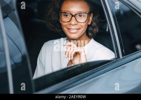 Lächeln, Geschäftsfrau, sitzen auf einem Rücksitz des Taxis und Wegsehen. Junge Unternehmer in einem Auto. Stockfoto