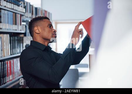 Kommissionierung Red Book. African American man in der Bibliothek nach Informationen suchen Stockfoto