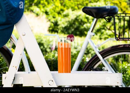 Glas Orangensaft im Garten auf Stuhl im Shabby Chic Stil. Verschwommen retro Bike im Hintergrund, umgeben von Natur. Ferienhäuser und hol Stockfoto