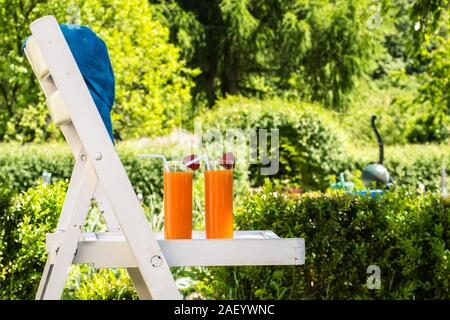 Zwei Gläser Orangensaft und Erdbeeren im Sommer Garten auf weißem Stuhl im Shabby Chic Stil. Umgeben von Natur. Ferienhäuser und Holi Stockfoto