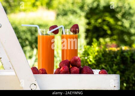 Zwei Gläser Orangensaft und Erdbeeren im Sommer Garten auf Stuhl im Shabby Chic Stil. Umgeben von Natur. Ferienhäuser und Urlaub in Stockfoto