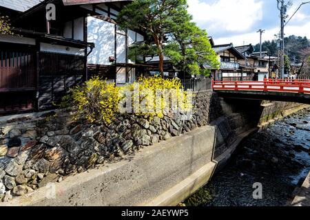 Takayama, Japan - April 9, 2019: Kleine rote Brücke von Enako Fluss in der Präfektur Gifu in Japan mit gelben Baum Blumen im Frühling großem Betrachtungswinkel Stockfoto