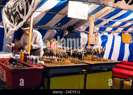 Kyoto, Japan - 9. April 2019: Maruyama Park in Gion dunklen Abend Nacht mit Street Food gegrillte Fisch aufgespießt sticks Koch Mann Menschen Stockfoto