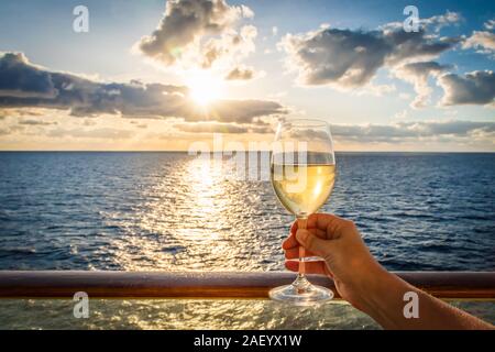 Bei Sonnenuntergang eine weibliche Hand Toast das Neue Jahr mit einem Glas Weisswein. Foto auf einem Balkon eines Kreuzfahrtschiffes mit Meerblick genommen. Stockfoto