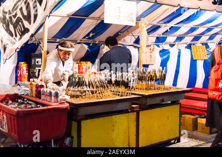 Kyoto, Japan - 9. April 2019: Maruyama Park in Gion Abend Nacht mit Street Food gegrillte Fisch aufgespießt sticks Koch Mann Menschen Stockfoto