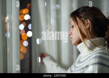 Traurige Frau allein Klagen stehen mit Blick auf die Lichter der Stadt durch ein Fenster in der Nacht zu Hause Stockfoto