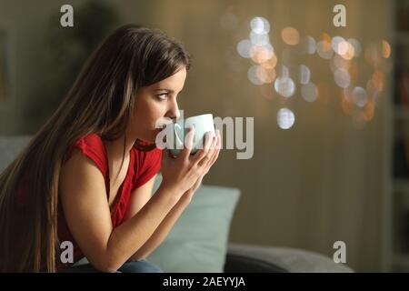 Seitenansicht Porträt einer Frau weg schauen Kaffee trinken sitzen auf einer Couch in der Nacht zu Hause Stockfoto