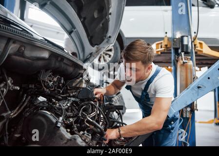 Männliche Mechanik auf den Job. Mitarbeiter in der blauen Uniform arbeitet im Automobil Salon Stockfoto