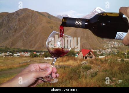 Des Menschen Hand gießen Rotwein aus der Flasche in wineglass im Dorf Mount Kazbek Stockfoto