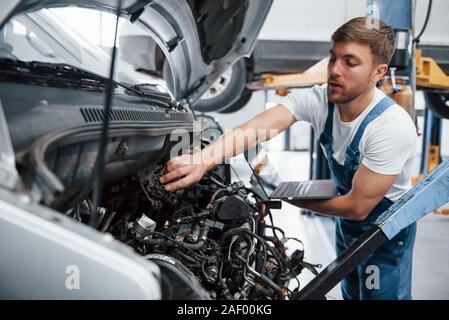 Silberfarbene Laptop in der Hand. Mitarbeiter in der blauen Uniform arbeitet im Automobil Salon Stockfoto