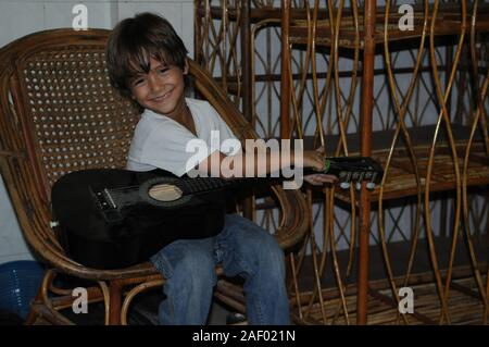 5 Jahre alten gemischten Rennen Junge (KAMBODSCHANISCHEN - Amerikanische) spielen eine akustische Gitarre sitzend auf Rattan. Phnom Penh, Kambodscha. © kraig Lieb Stockfoto