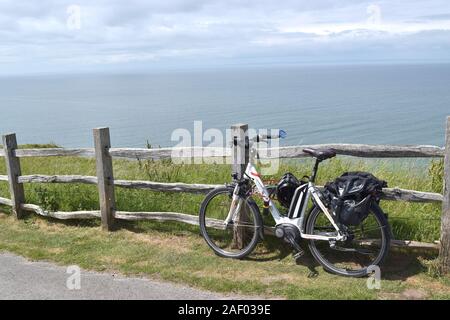 Fahrrad mit Helm und Beutel von einer malerischen Seenlandschaft an einem sonnigen Tag geparkt. Stockfoto