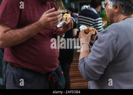 London - 20. August 2019: reifer Mann und Frau essen belegte Brötchen mit Wurst in Borough Market in London. Stockfoto