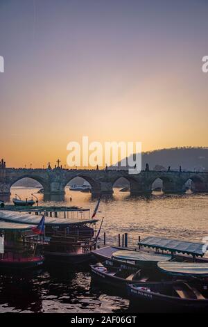 Prag, Tschechische Republik - Dez 2016: Sonnenuntergang über der Moldau in Prag, Tschechien, einschließlich Boote und die Silhouetten der Statuen auf der alte steinerne Karlsbrücke Stockfoto