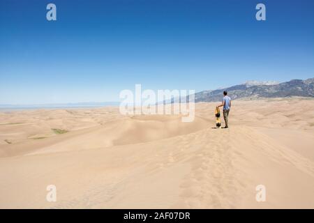 Junger Mann auf der Sanddüne mit Sand Board genießen den Blick in die Great Sand Dunes National Park, Colorado vereinigten Staaten von Amerika auf einer sonnigen da Stockfoto