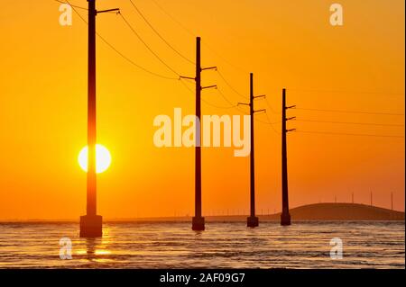 Elektrische Überlandleitungen über dem Atlantik, Silhouetted, während Golden Sunset, neben 7 Mile Bridge (Route 1), Marathon Key, Florida, USA Stockfoto