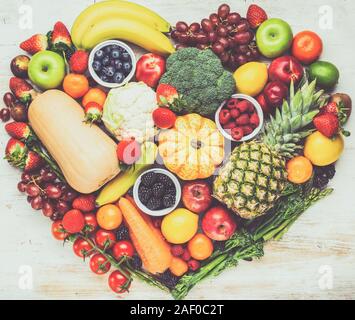 Herz aus gesunden rainbow Früchte Gemüse Beeren, Erdbeeren, Orangen, Pflaumen Trauben Brokkoli cauiliflower Mango kaki Ananas auf Holztisch, Ansicht von oben, getönt, selektiven Fokus Stockfoto