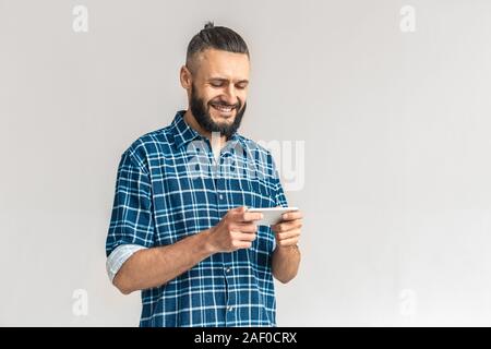 Freestyle. Kerl in kariertem Hemd stehen auf weißen spielen Spiel isoliert auf dem Smartphone lächelt glücklich Stockfoto
