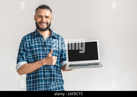 Freestyle. Kerl in kariertem Hemd stehen isoliert auf weißem angezeigt Bildschirm des Laptop kopieren Raum zeigen, Daumen hoch, lächeln, glücklich Stockfoto