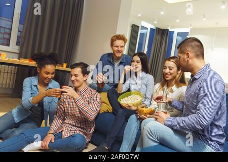 Eine Gruppe von Freunden, die party drinnen Spaß zusammen sitzen, trinken essen Stockfoto