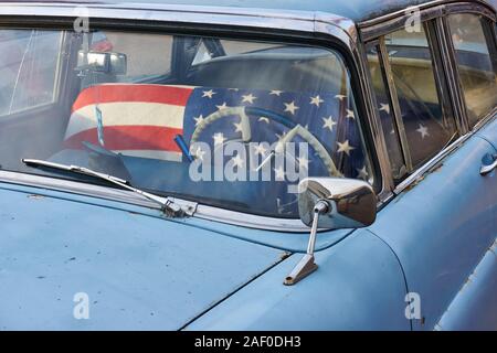 Nahaufnahme eines alten blauen, verwitterten und rostigen Oldtimers mit verchromtem Rückspiegel und amerikanischer Flagge auf dem Vordersitz Stockfoto