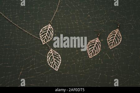 Die Natur inspirierte goldenen Accessoires. Mädchen Halskette und Ohrringe Paar auf Risse grüner Hintergrund Stockfoto