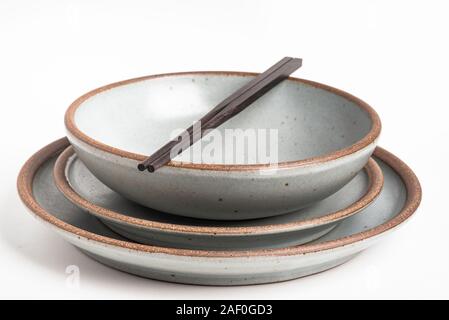 Ein paar orientalische schwarze hölzerne Stäbchen ruht auf einem Abendessen von texturierten Steinzeug Platten auf weißem Hintergrund. Stockfoto