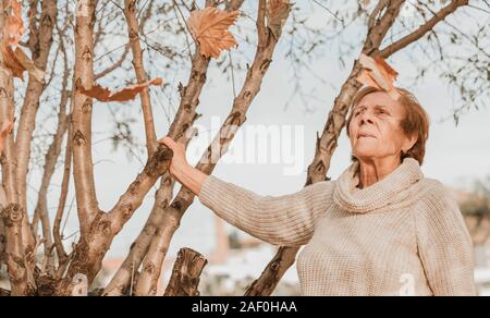 Blätter im Herbst fallen auf ältere Frau auf blauen Himmel Stockfoto