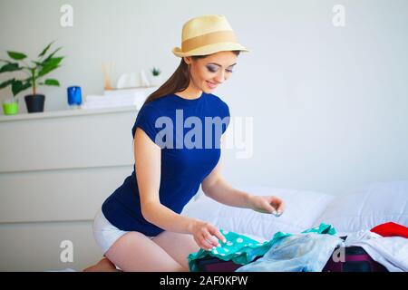 Ferienhäuser. Frau, die Vorbereitung für die Erholung. Junge schöne Mädchen sitzt auf dem Bett. Porträt eines lächelnden Frau. Glückliches Mädchen geht auf Urlaub Stockfoto