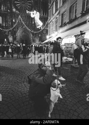 Straßburg, Frankreich - Dec 24, 2018: Schwarz-Weiß-Bild von einem Mann mit einer niedlichen Hund für ein Foto vor der Kathedrale Notre-Dame de Strasbourg Weihnachtsmarkt posing Stockfoto