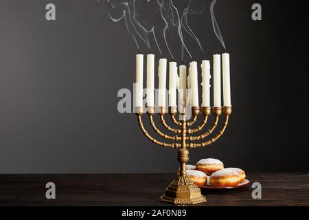 Delicious Doughnuts in der Nähe von Kerzen in der Menorah auf Holztisch auf Hanukkah isoliert auf Grau Stockfoto