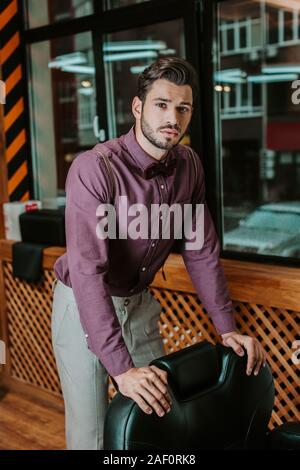 Schöne bärtige Friseur berühren Ledersessel im barbershop Stockfoto