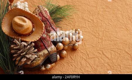 Weihnachten Cowboy Stiefel und Hut legen mit Kieferkegel, Gold Perlen, rustikale Beeren auf einem braunen strukturierten Hintergrund mit Schreibfläche Stockfoto