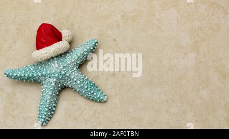 Türkis starfish tragen Santa Hut in der Nähe auf einer festlichen Tan sandy Hintergrund mit Kopie Raum isoliert Stockfoto